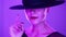 Mature charming woman posing with black hat on violet studio background with colorful light. Femme fatale, stylish