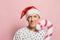 Mature cheerful man looking at the camera on a pink background. Smiling elderly guy in a santa hat