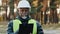 Mature concentrated forestry engineer technician forester in protective helmet stands in park assesses situation makes