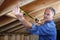 Mature construction worker measuring distance between rafter beams.