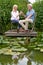 Mature Couple Celebrating With Champagne Sitting On Chairs On Wooden Jetty By Lake