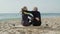 Mature couple embracing while sitting on surfboard on seashore
