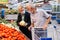 Mature couple in mask and gloves with covid protection picks tomatoes in vegetable section of supermarket