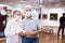 Mature couple in mask protecting against covid examines paintings on display in hall of art museum