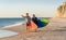 Mature couple surfers with surfboard having fun on empty remote beach enjoying outdoors lifestyle