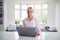 Mature Disabled Woman With Crutches At Home Working On Laptop On Kitchen Counter