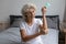 Mature elderly 60s woman applying cream on elbow in bedroom