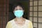 Mature or elderly Chinese woman with face covered with medical face mask outside her home