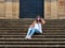 Mature and elegant woman sits on the steps of the cathedral in Baeza, Jaen, Spain with mask and transparent umbrella