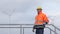 Mature engineer with protective workwear passing by in front of wind turbines