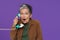 Mature excited, shocked grey haired woman chatting or gossiping on the phone holding retro telephone handset wearing