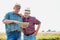 Mature farmer showing digital tablet to senior farmer in field