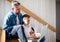 Mature father with small son sitting on the stairs indoors, using laptop.