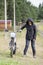 Mature female dressed black jacket with hood on head standing with dirt motorbike on country road in village, portrait