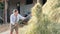 Mature female farmer turns the hay for cow with pitchfork on the backyard of farm. Growing livestock is a traditional direction of