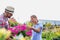 Mature gardener showing flowers on pot to woman buyer in shop