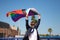 Mature gay man, executive, grey-haired, bearded, sunglasses, jacket and tie, waving the new lgbtiq+ pride flag in the wind under a