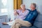 Mature good-looking well dressed couple sitting in sofa in day light from big window and yellow curtains in living room