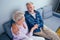 Mature good-looking well dressed couple sitting in sofa in day light from big window and yellow curtains in living room