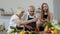 Mature grandparents couple cutting vegetables for salad, listening recipe from girl with tablet