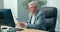 Mature, gray-haired, elegant businessman sits in office at the computer, completes company documents, checks data in the