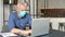 Mature gray-haired male employee wearing medical mask is using laptop at the office