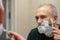 Mature gray-haired man restyling his beard himself at home using razor