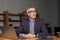 Mature grey haired businessman or entrepreneur in eye glasses and suit is sitting by the laptop in his office