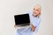 Mature grey-haired woman smiling and showing blank screen of laptop isolated