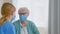 Mature grey haired woman wearing protective mask talks to nurse at appointment with doctor in room