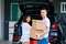 Mature happy Asian married couple carrying cardboard boxes from car trunk at new home