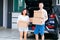 Mature happy Asian married couple carrying cardboard boxes from car trunk at new home.