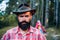 Mature hipster with beard. Brutal man with beard in hat. Brutal brunette bearded man in hat on a background of trees
