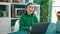 Mature hispanic woman with grey hair using laptop smiling at dinning room