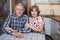 Mature husband and wife sitting together at the kitchen table and looking at camera