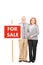 Mature husband and wife standing by for sale sign