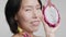 Mature Korean Lady Holding Dragon Fruit Near Face, Gray Background