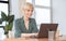 Mature Lady Working On Laptop In Earphones Sitting In Office