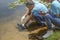 mature male biologist injecting microchips to reproduce fish in the river and a young woman helper record data