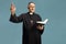 Mature male priest reading a prayer from the bible and gesturing with hand