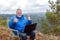 Mature male tourist with a laptop on a rock.