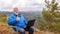 Mature male tourist with a laptop on top of a mountain.