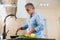 Mature man in blue shirt cooking on modern kitchen. Light cozy room on background. Concentrated man standing by stove