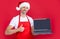 mature man in christmas santa hat and red apron presenting laptop. thumb up