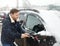 A mature man cleans his car with a brush after a snowfall. Snowdrift after a snowstorm on the hood of the automobile