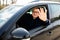 Mature man driving a car is happy and shows his satisfaction by smiling and raising his hand to greet