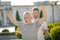 Mature man frowning, raising hands with dumbbells, bearded instructor assisting him