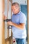 Mature man himself installs the door hinges with screwdriver