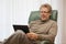 Mature man looking at a tablet while sitting in a chair in a bright living room