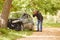 Mature Man Next To Car Crashed Into Tree Inspecting Accident Damage And Calling Emergency Services